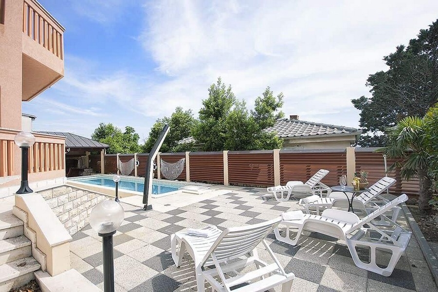 Piscine avec transats sur la terrasse en pierre à damier
