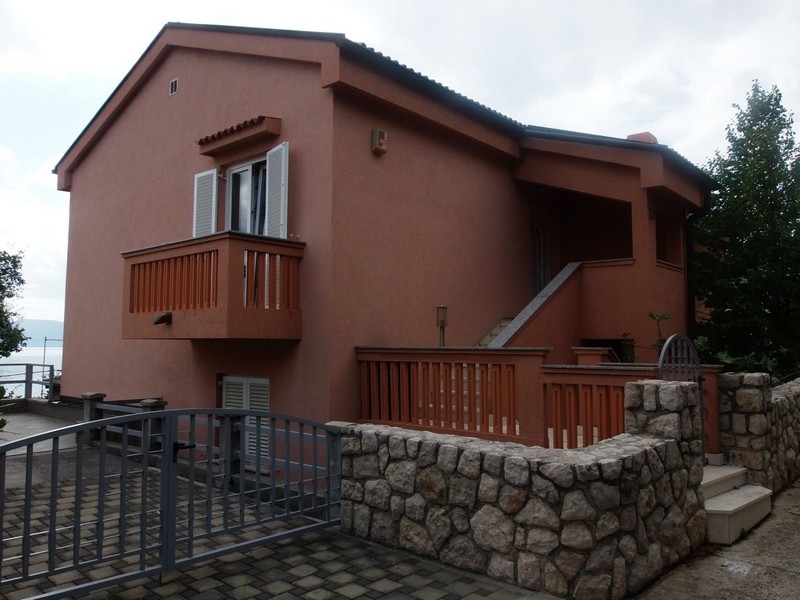 Côté de la maison avec balcon en bois et terrasse au-dessus du mur