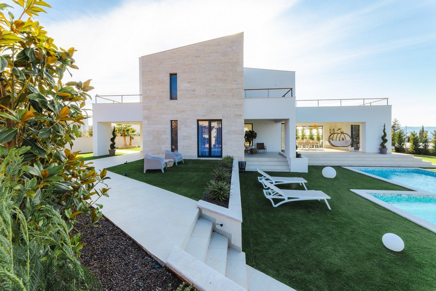 Villa à façade en pierre naturelle et transats sur la pelouse