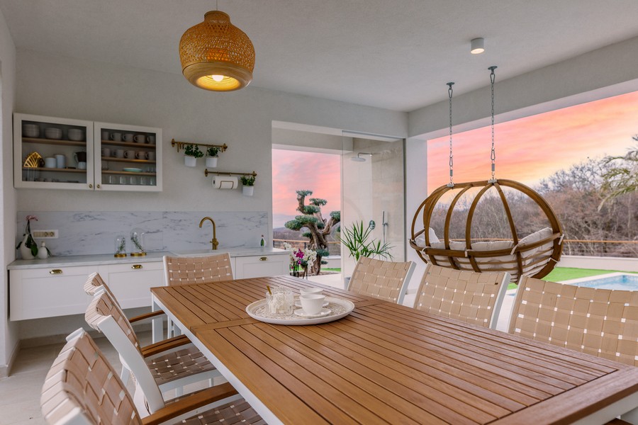 Coin repas avec table en bois et fauteuil suspendu à la lumière du soir