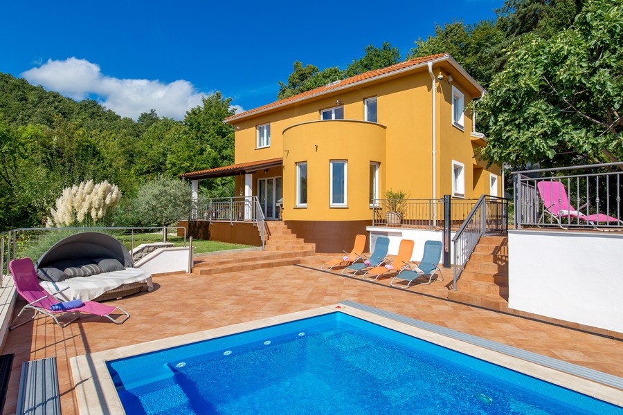 Villa jaune avec partie ronde et bains de soleil au bord de la piscine