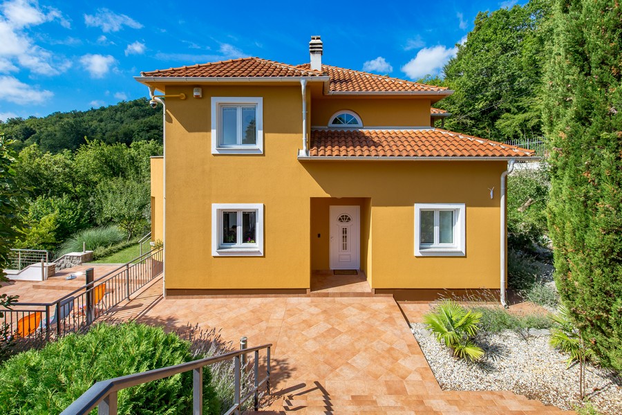 Côté entrée de la villa jaune avec toit en tuiles et cyprès