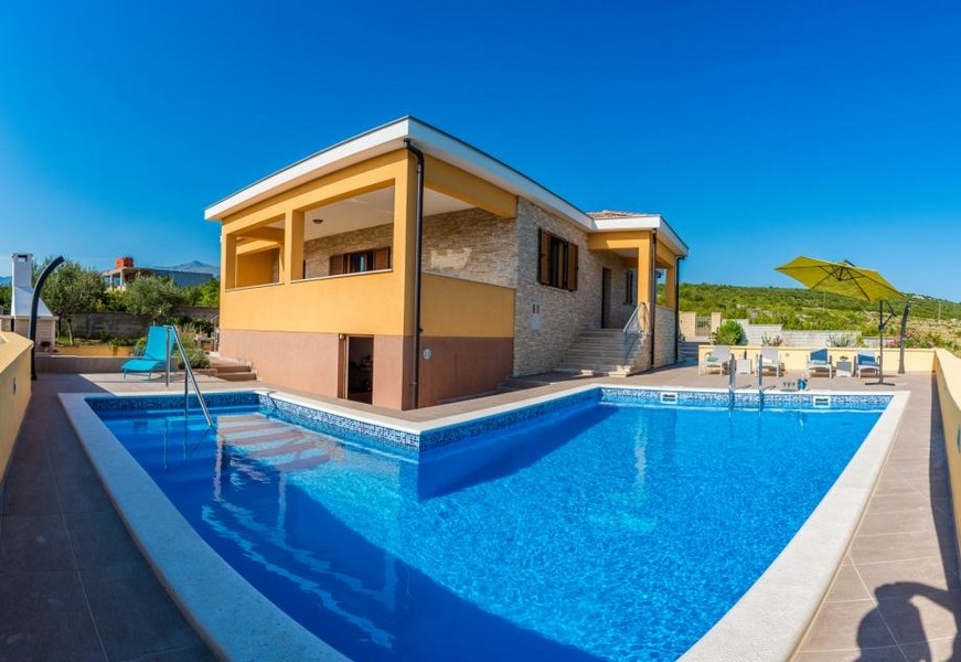 Grande piscine devant la maison avec pierre naturelle et parasol