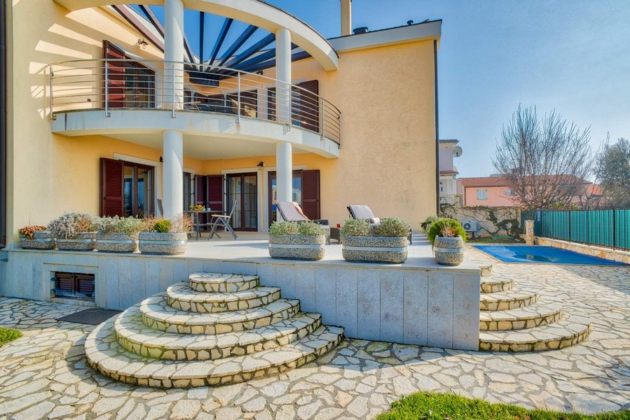 Villa avec balcon rond et escalier en pierre naturelle menant à la piscine