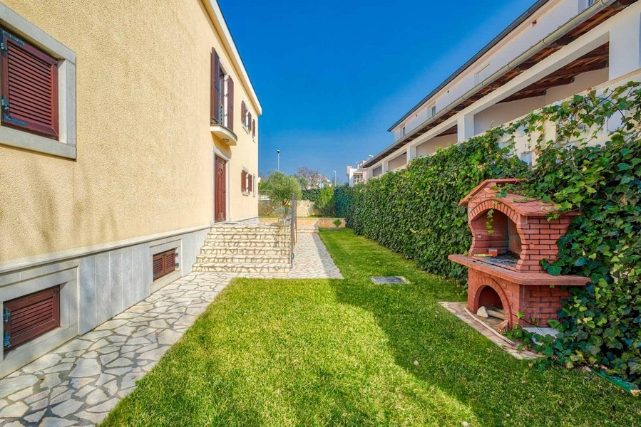 Bande de pelouse le long de la maison avec barbecue maçonné près de la haie