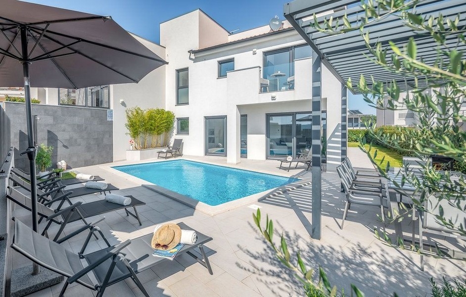 Piscine avec parasol et transats entre des branches d'olivier