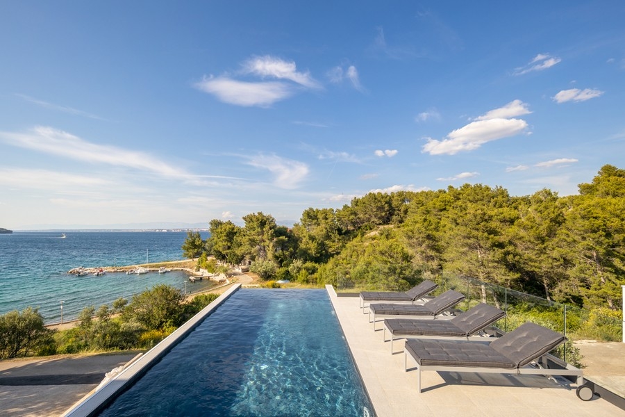 Piscine à débordement avec rangée de transats au-dessus de la promenade en bord de mer