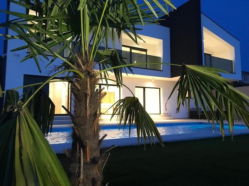 Villa éclairée avec piscine derrière le palmier le soir
