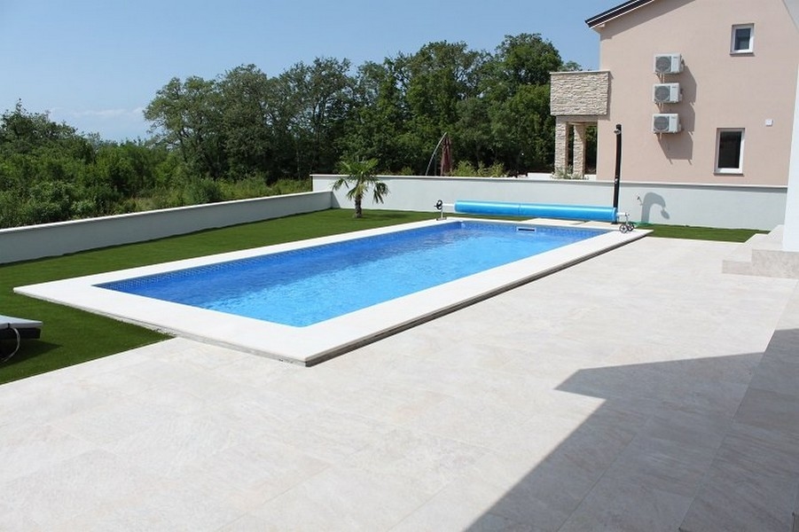 Longue piscine sur la terrasse carrelée à côté de la pelouse