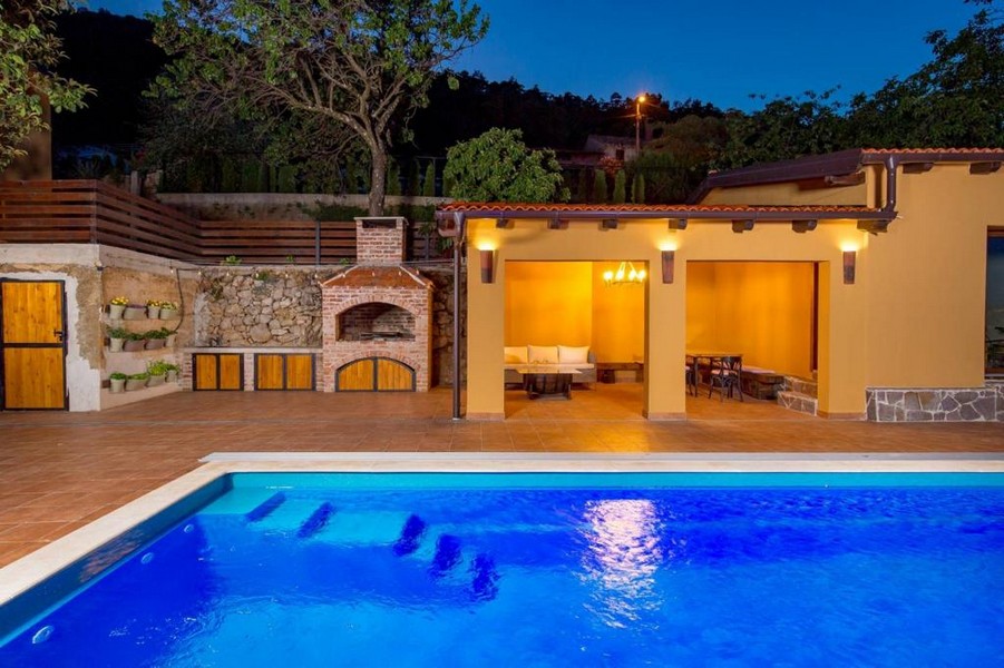 Piscine éclairée devant la cuisine d'été avec cheminée maçonnée