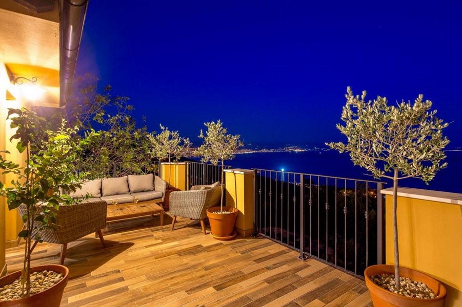 Terrasse en bois avec canapé en rotin et oliviers le soir