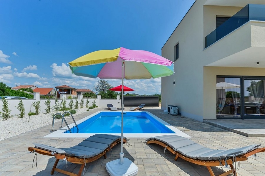 Piscine avec parasols colorés et bains de soleil à côté de la maison jumelée