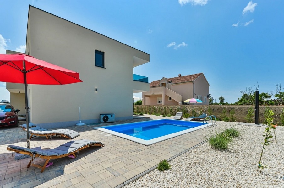 Piscine avec bains de soleil et parasol rouge à côté de la maison