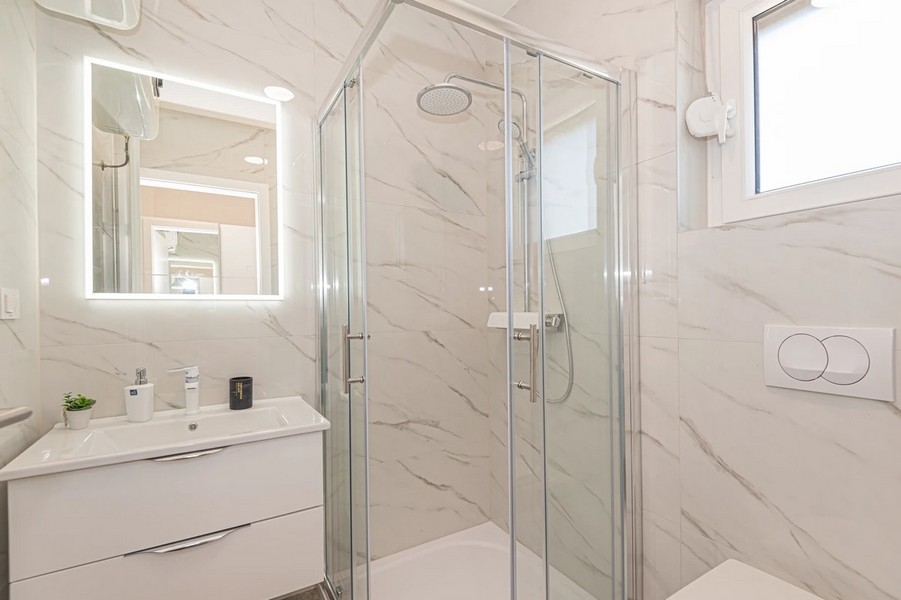 Salle de bains aspect marbre avec douche d'angle et miroir éclairé