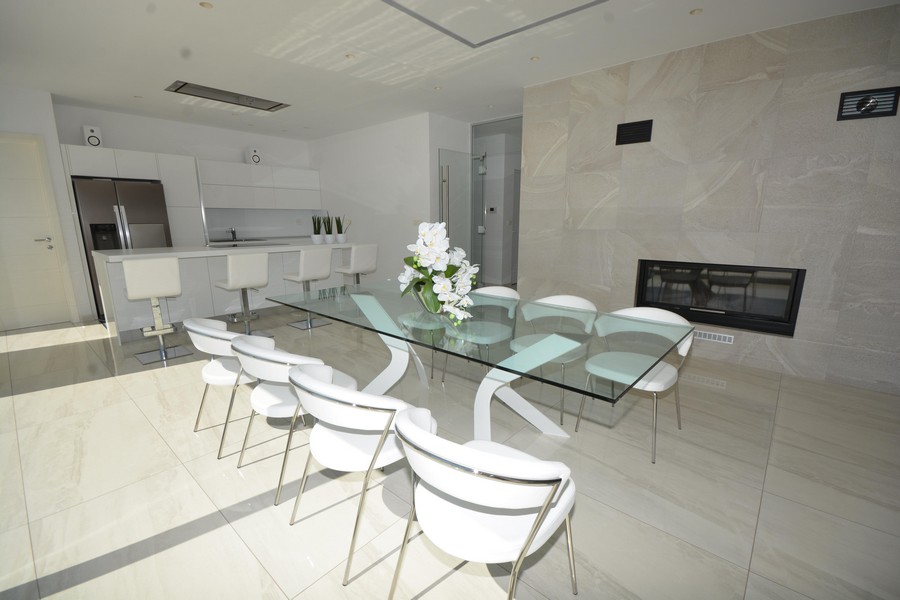 Table en verre avec chaises blanches devant la cheminée et la cuisine ouverte