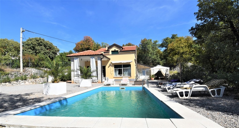 Longue piscine avec bains de soleil devant la maison jaune