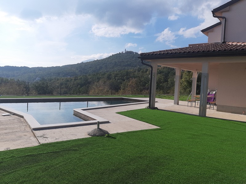 Piscine avec gazon synthétique et terrasse devant les collines boisées