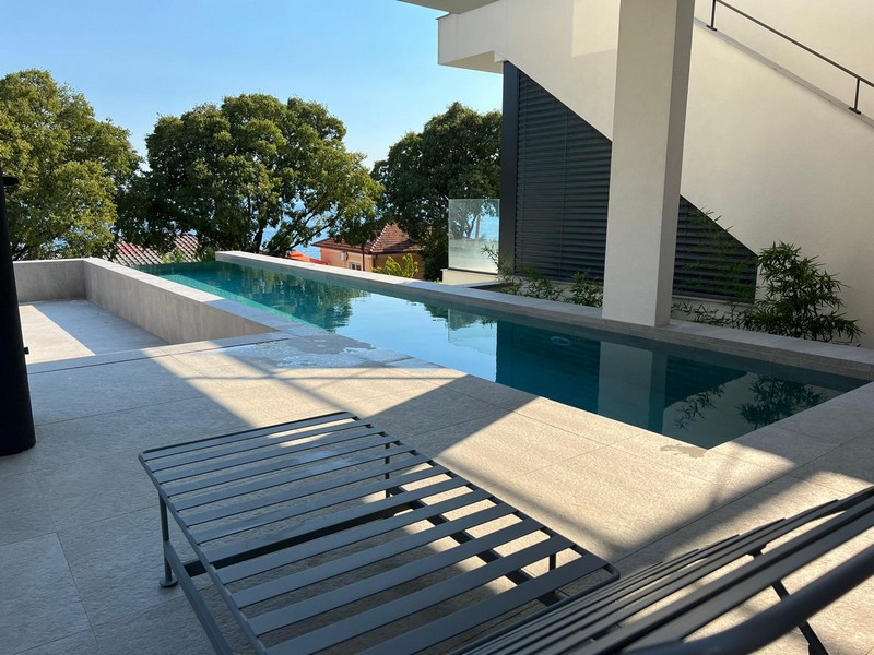 Piscine à débordement avec bains de soleil à côté de la façade claire