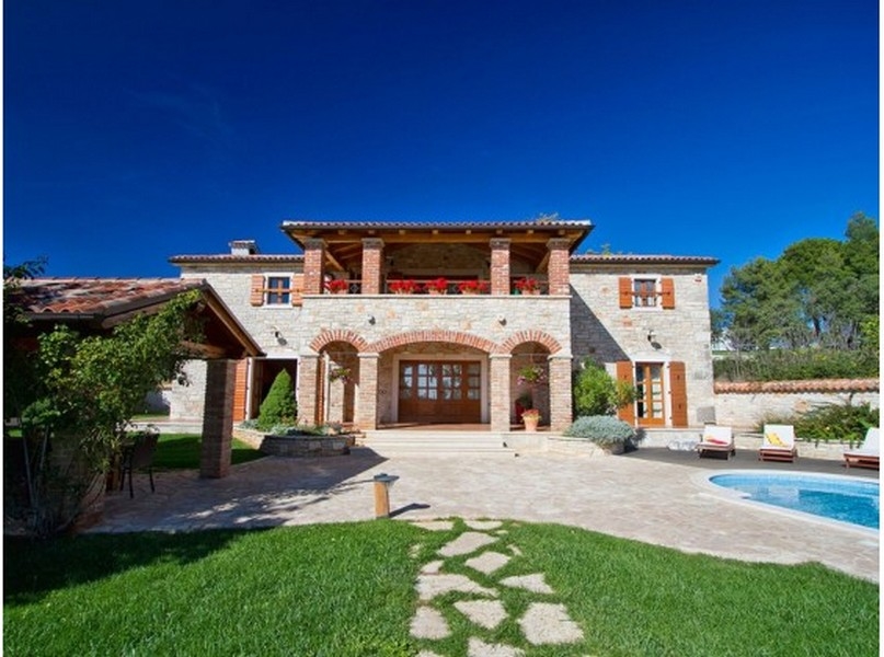 Maison en pierre avec arcs en briques et balcon au-dessus du jardin