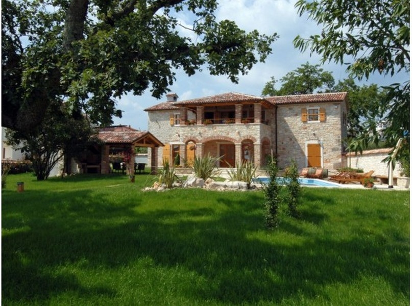 Maison en pierre avec arcades et piscine derrière la pelouse