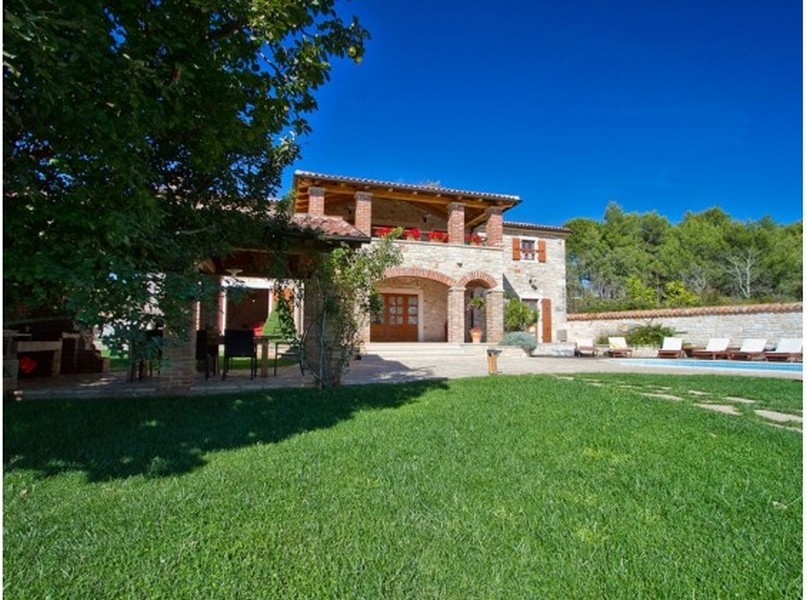 Villa en pierre avec loggia et jardinières au-dessus de la pelouse