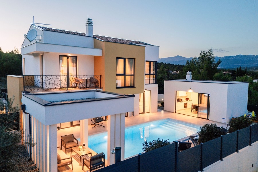 Vue extérieure avec balcon, terrasse et piscine le soir