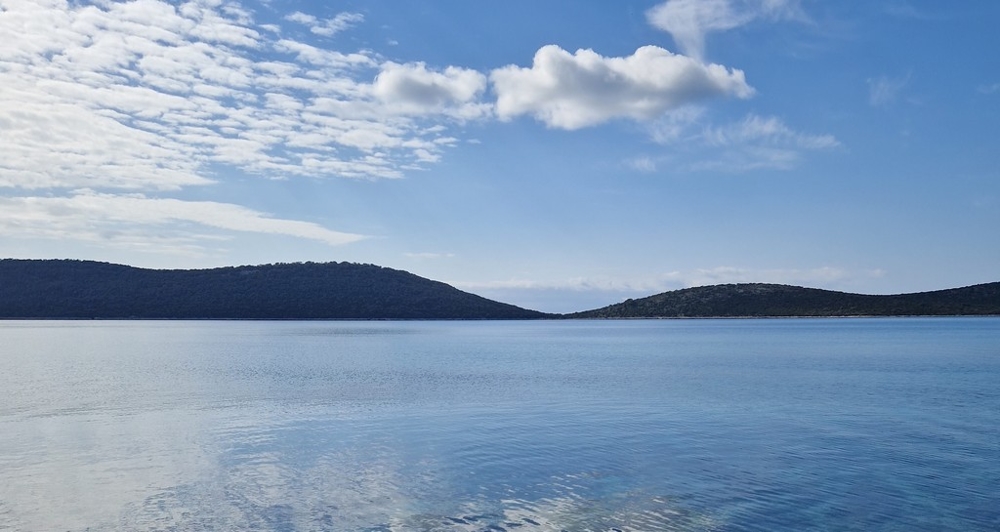 Surface d'eau calme devant des collines boisées sous des moutons de nuages