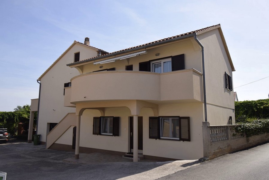 Maison jaune avec balcon rond et escalier extérieur menant à l'appartement