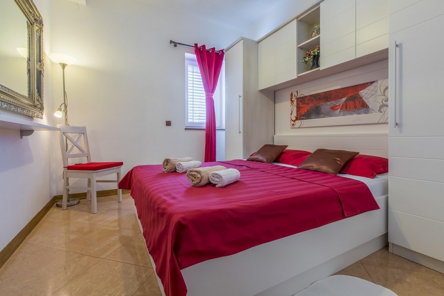 Chambre avec housse de couette rouge et mobilier blanc dans une maison à plusieurs logements croate en bord de mer