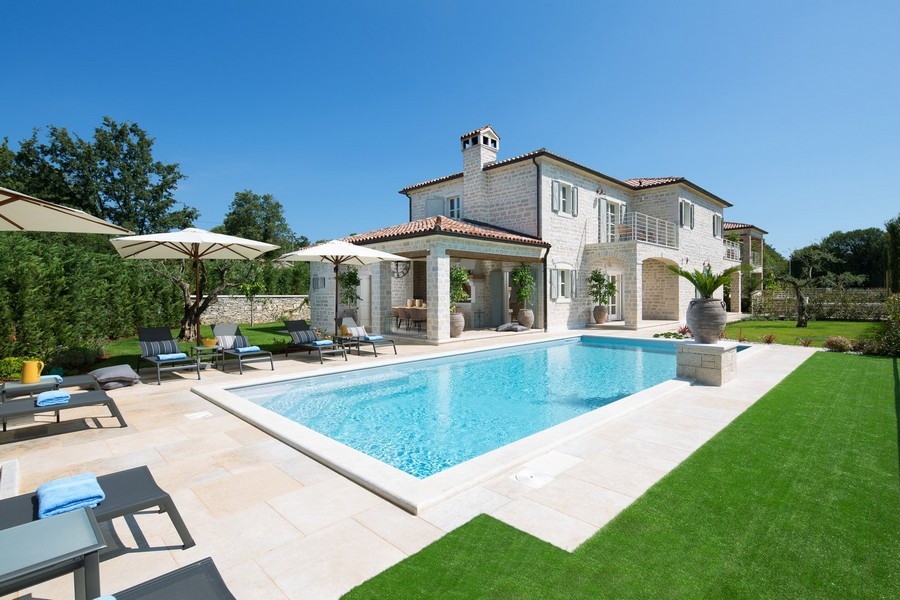 Vue claire et ensoleillée d'une villa croate avec piscine, parasols et chaises longues.