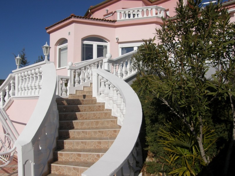 Façade de la villa rose en Croatie avec escalier blanc sinueux et végétation méditerranéenne