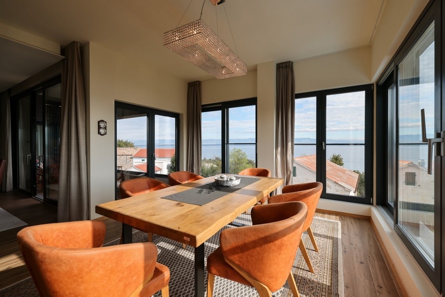 Coin repas avec table en bois, chaises orange et vue mer