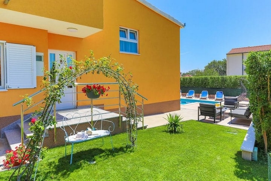 Jardin entretenu avec pelouse et arche de rosiers de l'immeuble de rapport à Kaštel Lukšić, Croatie
