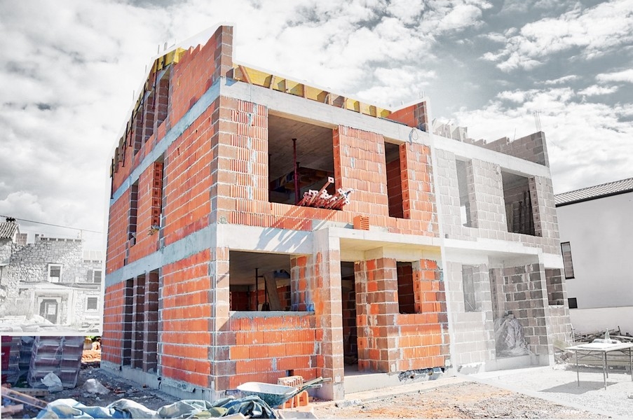 Maison jumelée à moitié achevée en phase de construction avec murs en briques visibles et ouvertures pour fenêtres et portes