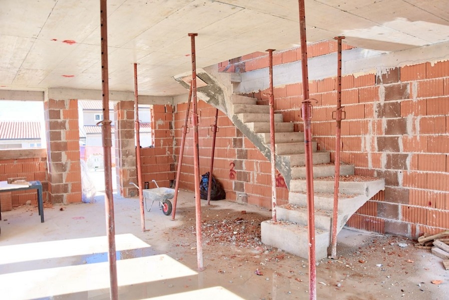 Vue intérieure de la maison jumelée en construction avec escalier en béton et murs en briques