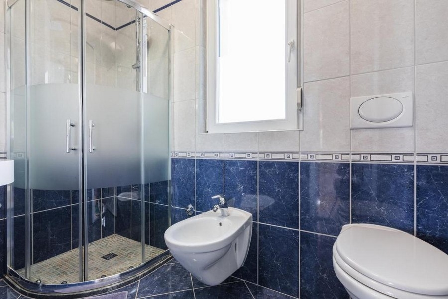 Salle de bains dans un bien en Croatie, immeuble collectif avec vue mer, avec douche d'angle, bidet et WC, murs clairs et carrelage bleu foncé
