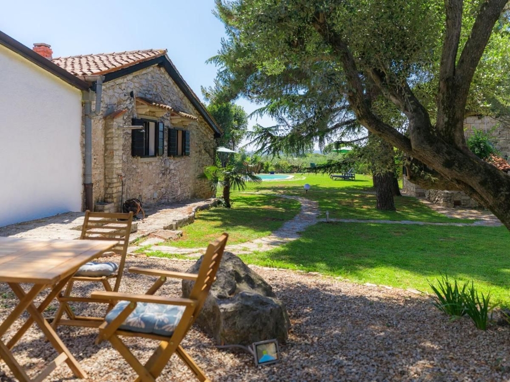 Chemin à travers un jardin ombragé menant à un charmant bâtiment en pierre, typique des biens immobiliers en Croatie