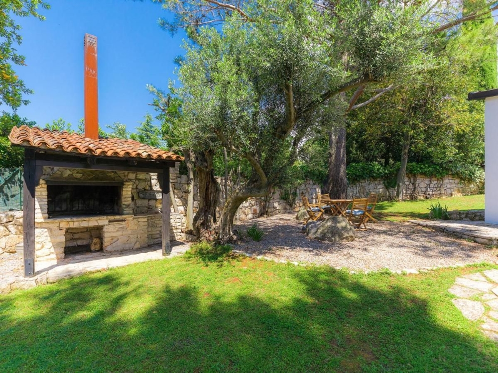 Coin barbecue rustique en plein air avec places assises sous des oliviers, caractéristique des biens immobiliers en Croatie