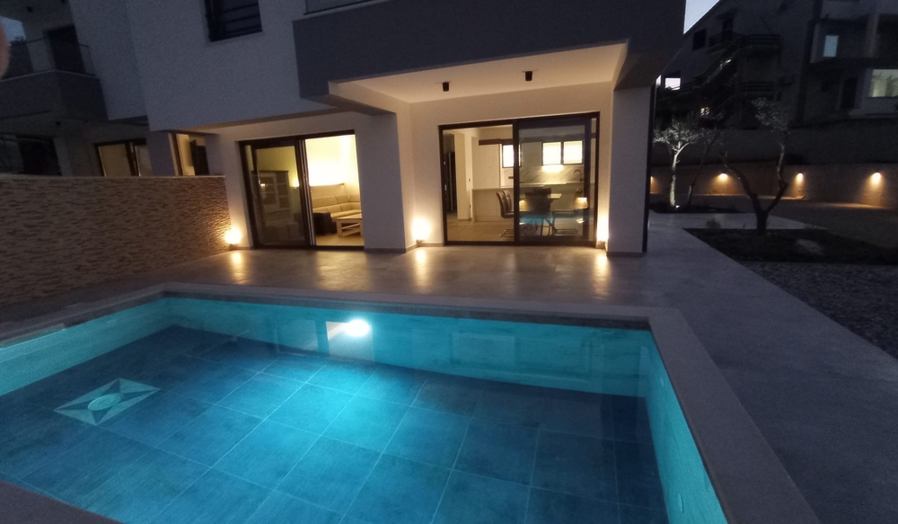 Vue au crépuscule de la terrasse et de la piscine d'un bien en Croatie, l'éclairage intérieur crée une atmosphère accueillante.