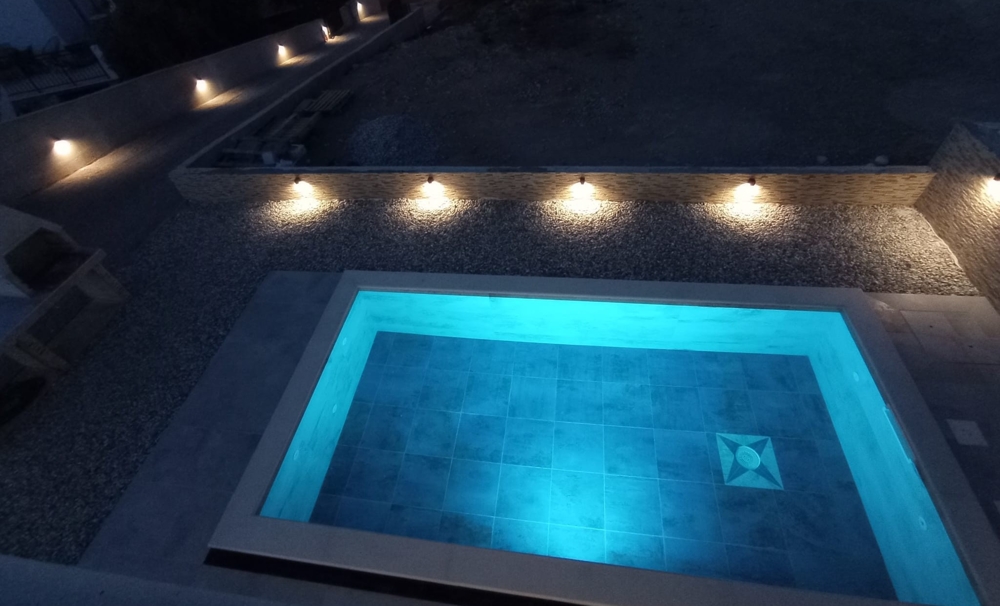 Vue de nuit d'une piscine avec éclairage bleu et vue partielle du bien en Croatie à l'arrière-plan.