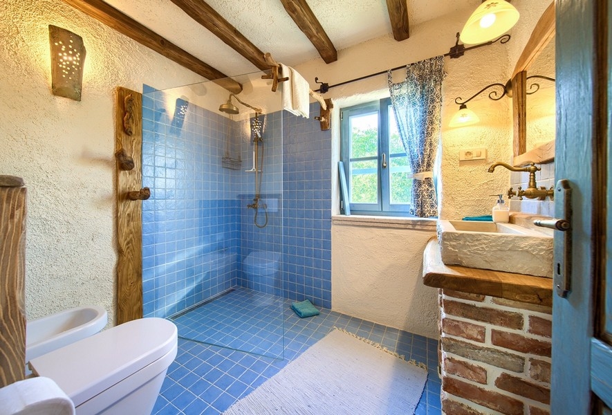 Salle de bains avec carrelage bleu, poutres en bois et douche de pluie