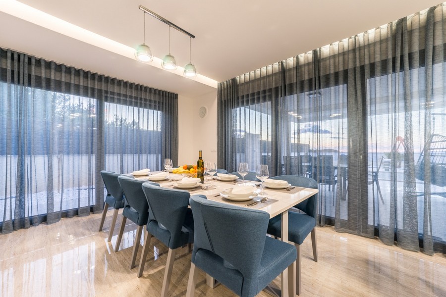 Élégant espace repas avec de grandes fenêtres qui laissent entrer la lumière naturelle et offrent une vue sur le bien de vos rêves en Croatie.