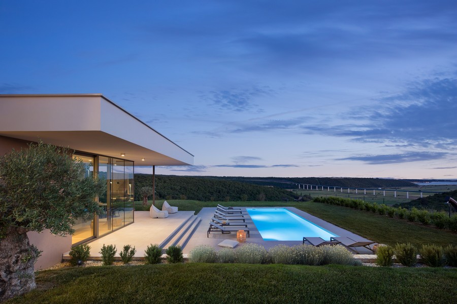 Piscine à la lumière du soir à côté de la façade vitrée avec olivier