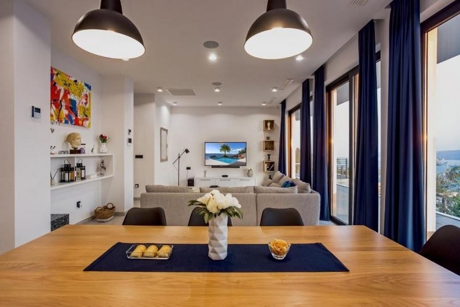 Salon avec grand canapé, téléviseur à écran plat et vue mer par de grandes fenêtres