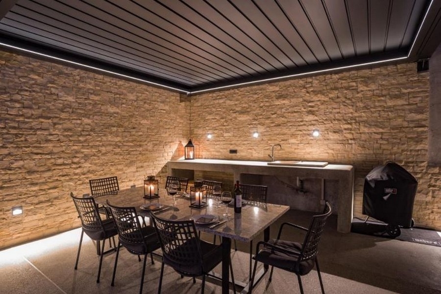 Espace extérieur couvert avec coin repas et barbecue, entouré de murs en pierre