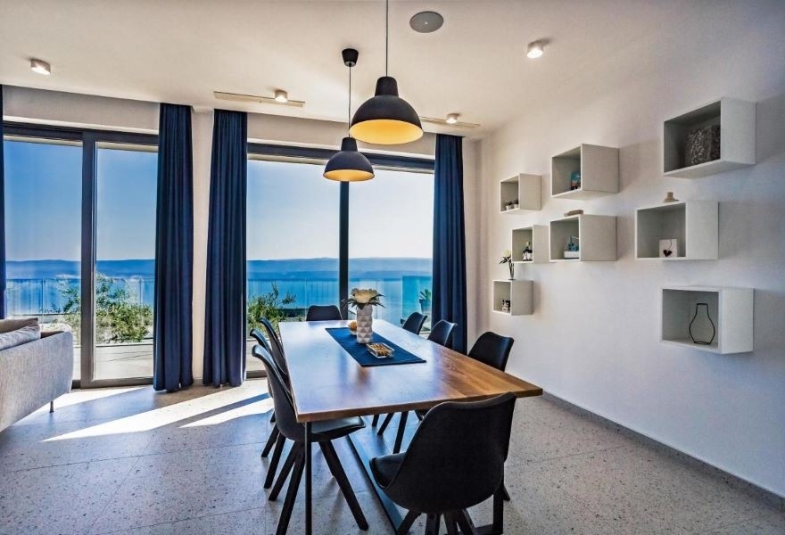 Salle à manger avec table en bois moderne, chaises noires et vue panoramique sur la mer