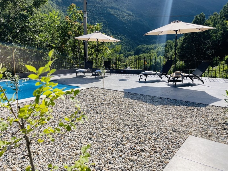 Solarium au bord de la piscine avec bains de soleil et parasols, entouré de nature verdoyante