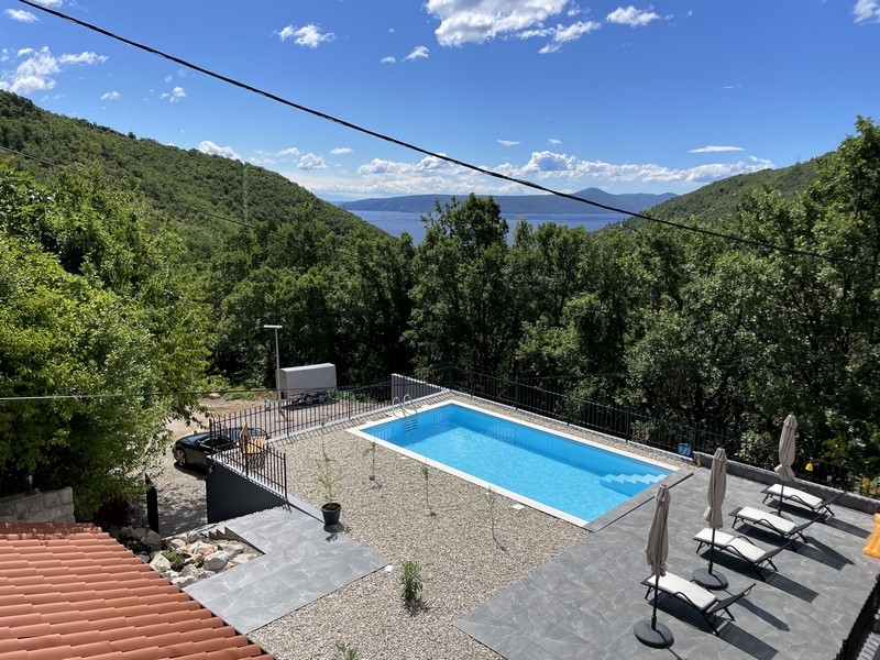 Piscine avec transats entre des pentes boisées avec vue mer