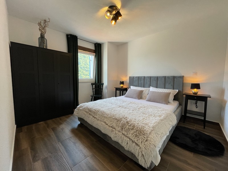 Chambre avec lit gris, armoire noire et deux tables de chevet, éclairée par une lumière chaude