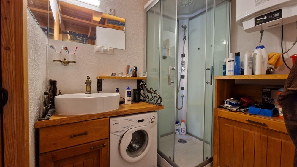 Salle de bains avec cabine de douche, lave-linge et étagères en bois.